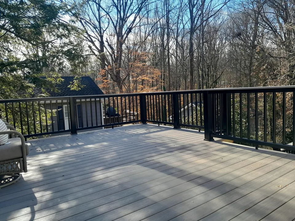 Wood deck boards with black railing and trees in the background