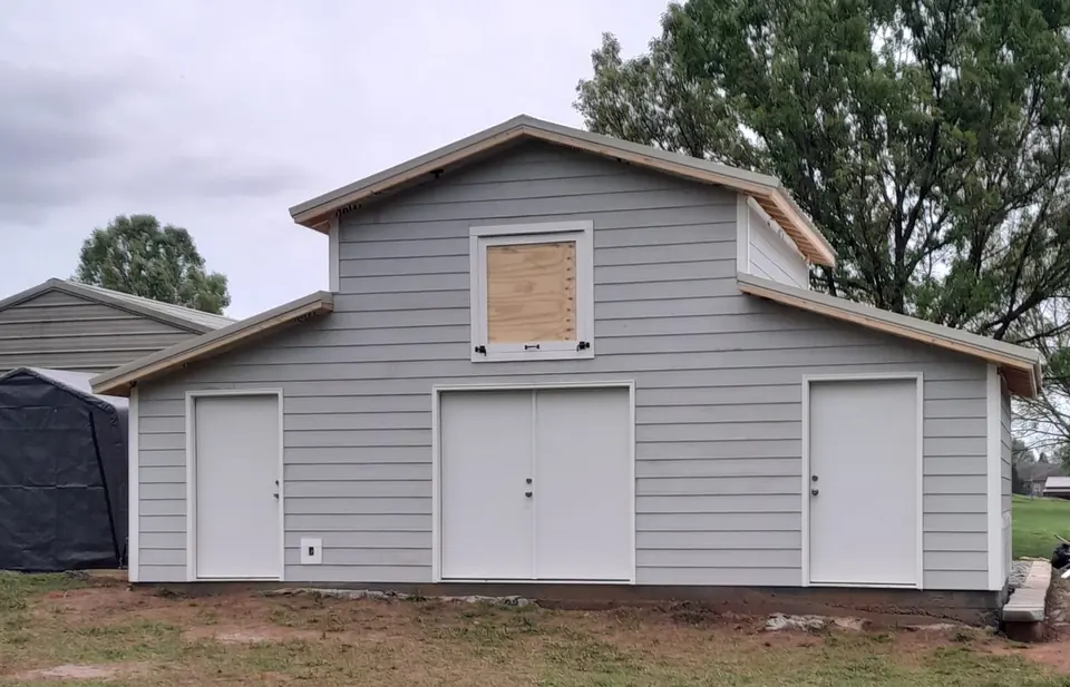 Gray outbuilding front with double doors and upper opening